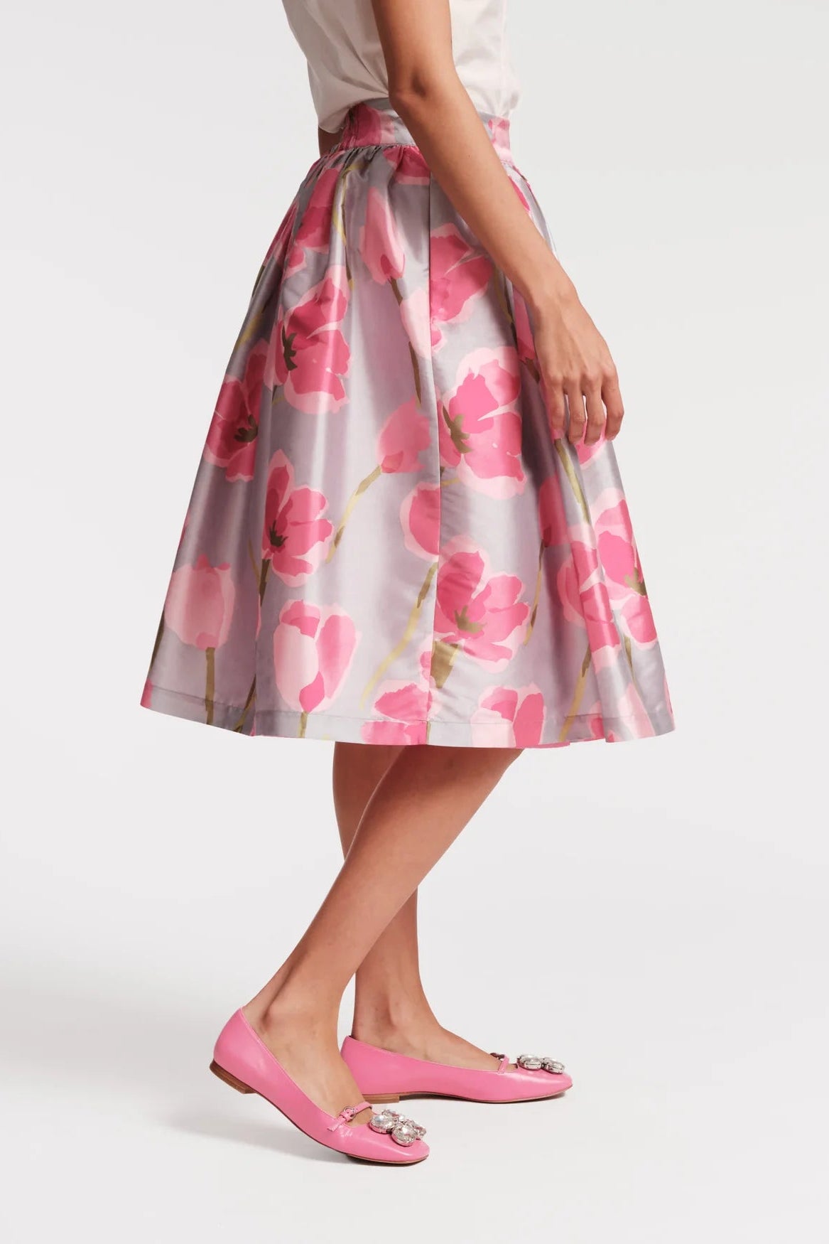 Person wearing a floral skirt with pink shoes on a white background