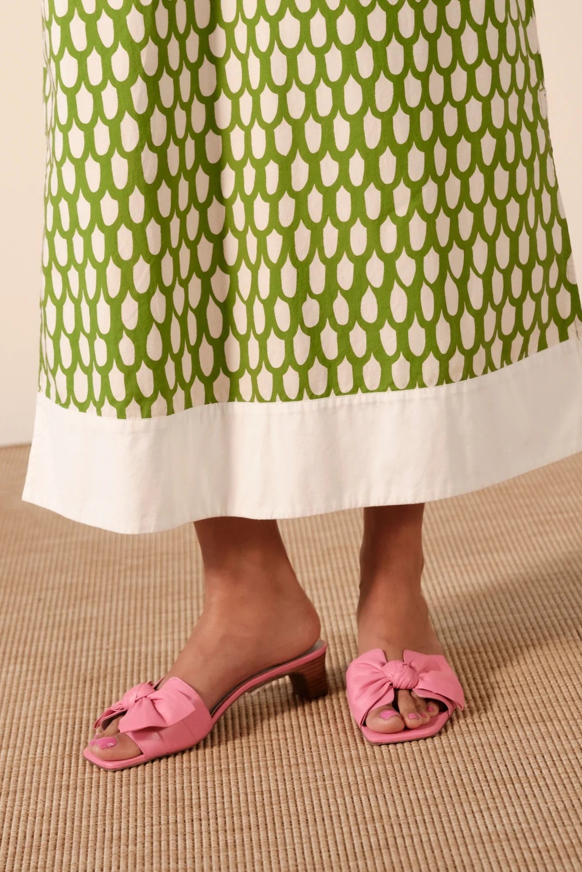 Person wearing a green and white patterned skirt with pink sandals on a beige floor.