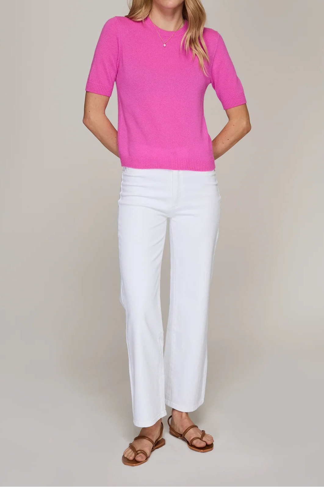 Woman wearing a pink top and white pants against a plain background