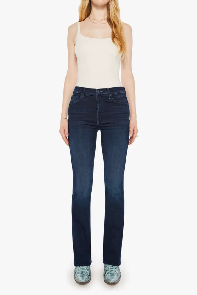 A woman modeling dark blue skinny jeans with a white ribbed tank top and tortoiseshell sunglasses, standing against a plain white background.