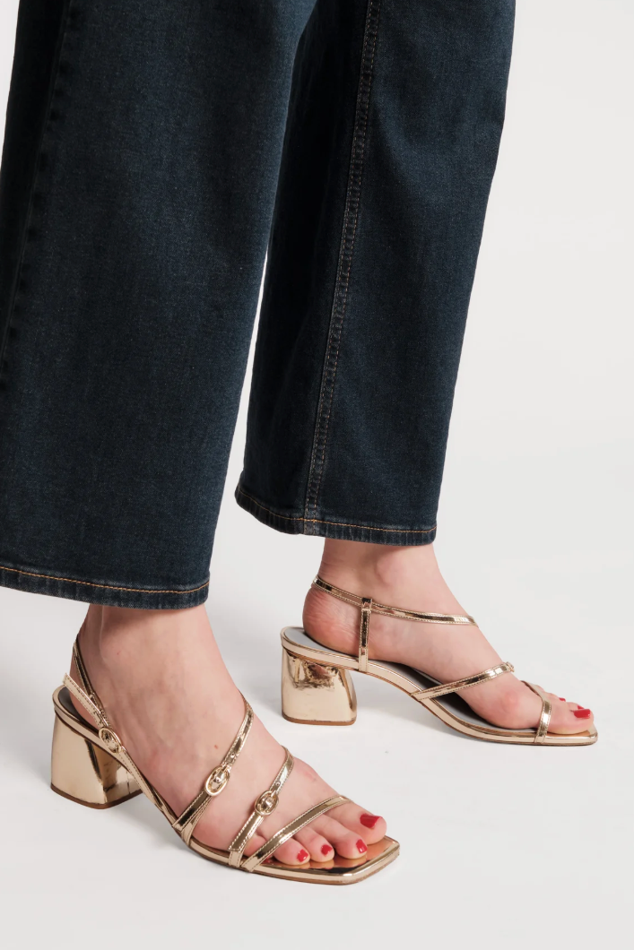 Gold high-heeled sandals worn with dark jeans on a light background