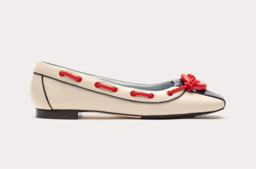 White flat shoe with red accents on a light gray background