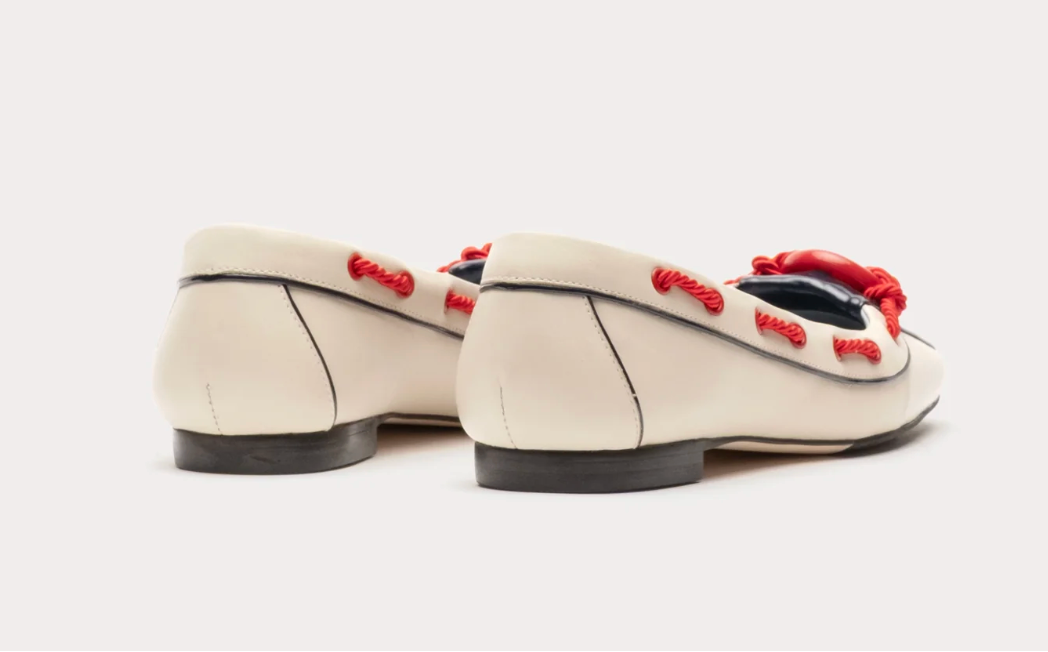 Pair of cream-colored loafers with red accents on a white background