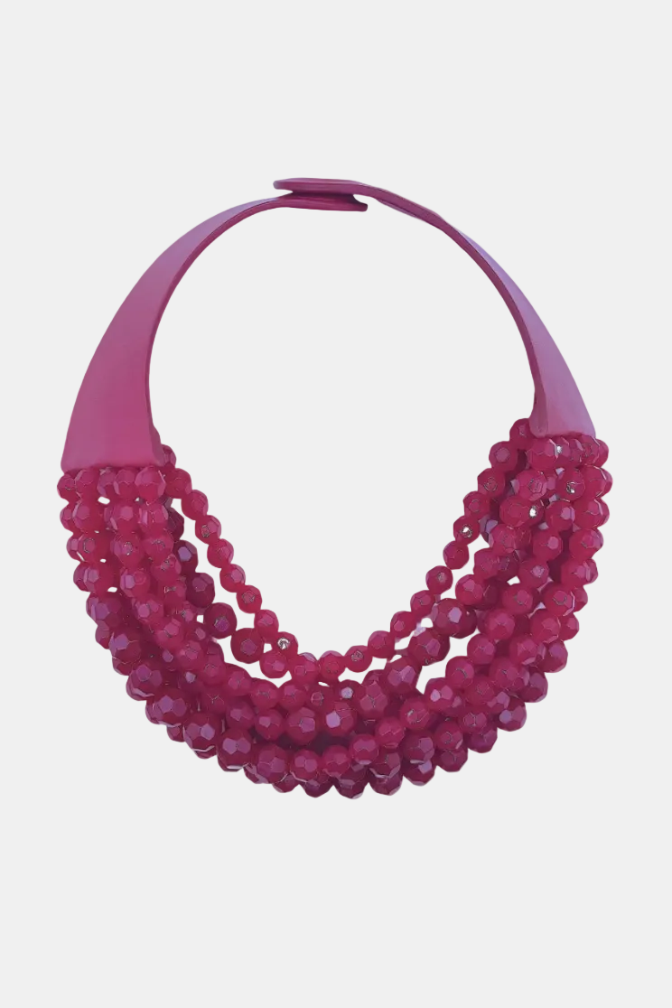 A multi-strand statement necklace featuring faceted magenta beads draped over a solid magenta collar band, shown against a plain white background.