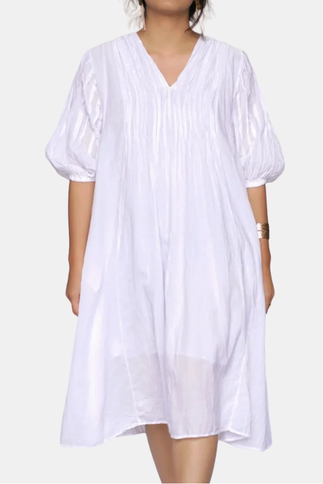 A woman wearing a loose white short-sleeve dress with a V-neckline and gathered puff sleeves, photographed against a plain white background.