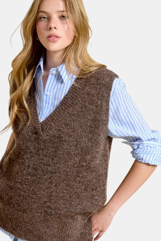 A woman wearing a brown knit sweater vest over a light blue and white striped button-down shirt, posed against a white background with a faint blue grid pattern.