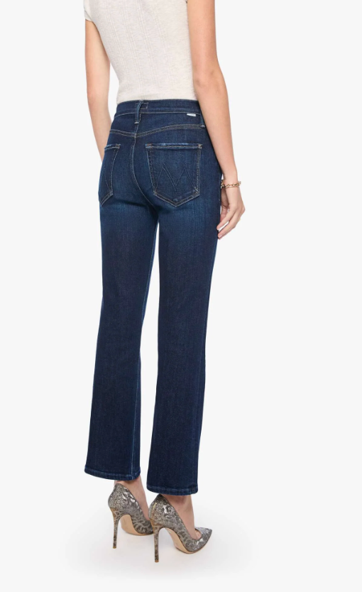Rear view of a model wearing dark blue flare jeans, a light beige top, and patterned high heels against a plain white background.