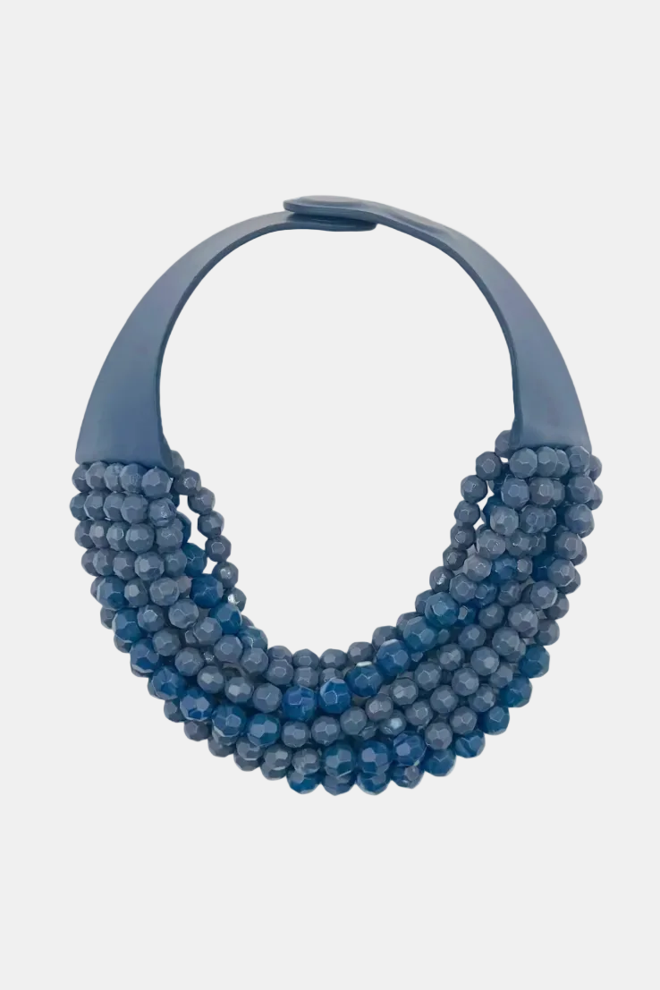 A chunky statement necklace featuring a wide, matte slate-blue collar band and multiple layered strands of faceted blue beads, shown against a plain white background.