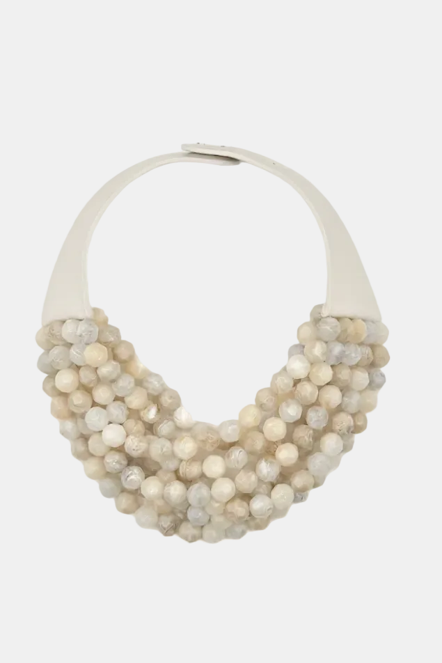 A statement collar necklace featuring multiple tiers of textured, faceted round beads in cream, beige, and light gray, attached to a wide, smooth off-white collar band.