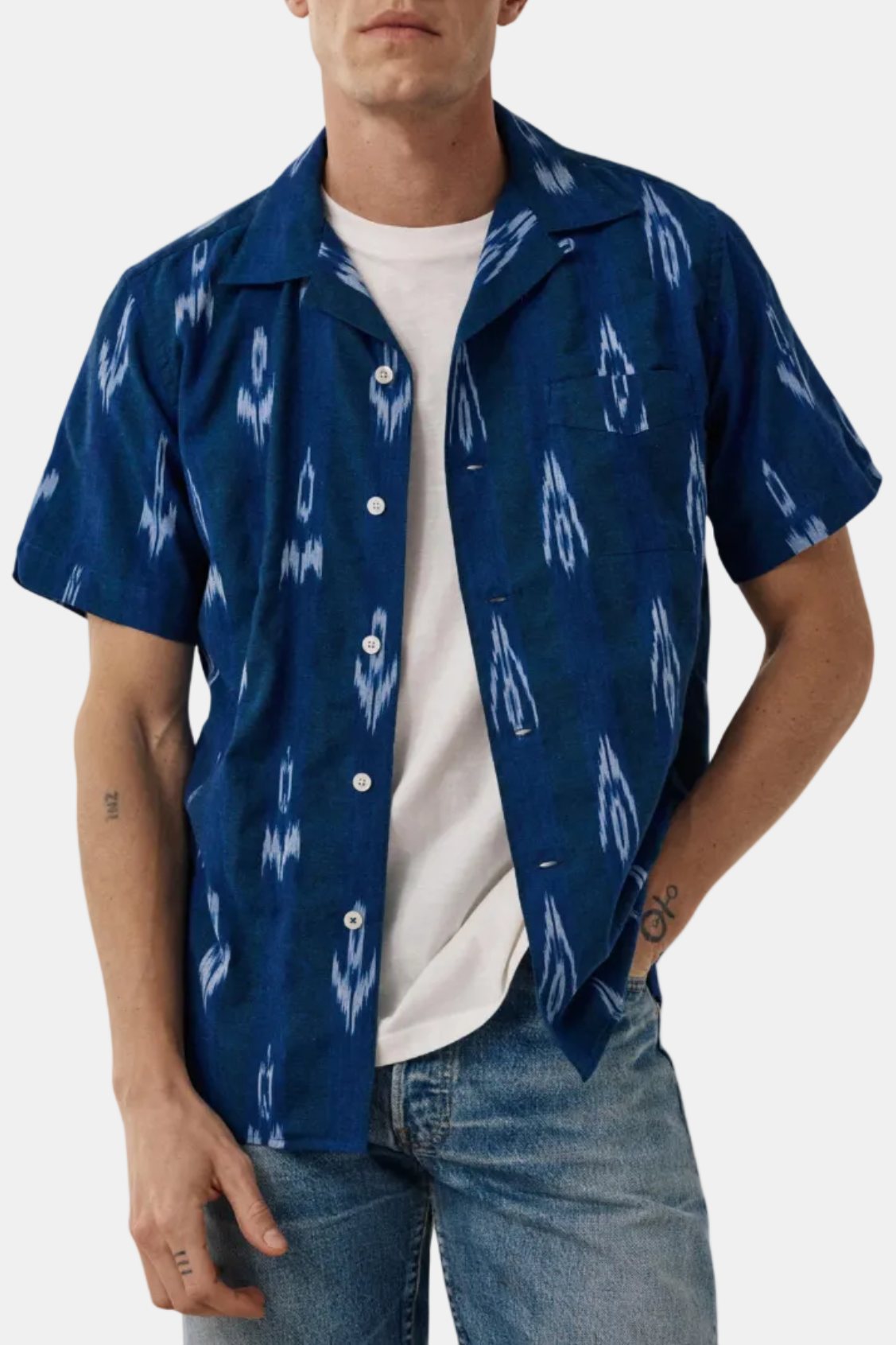 Man wearing a blue patterned shirt over a white t-shirt with jeans on a white background