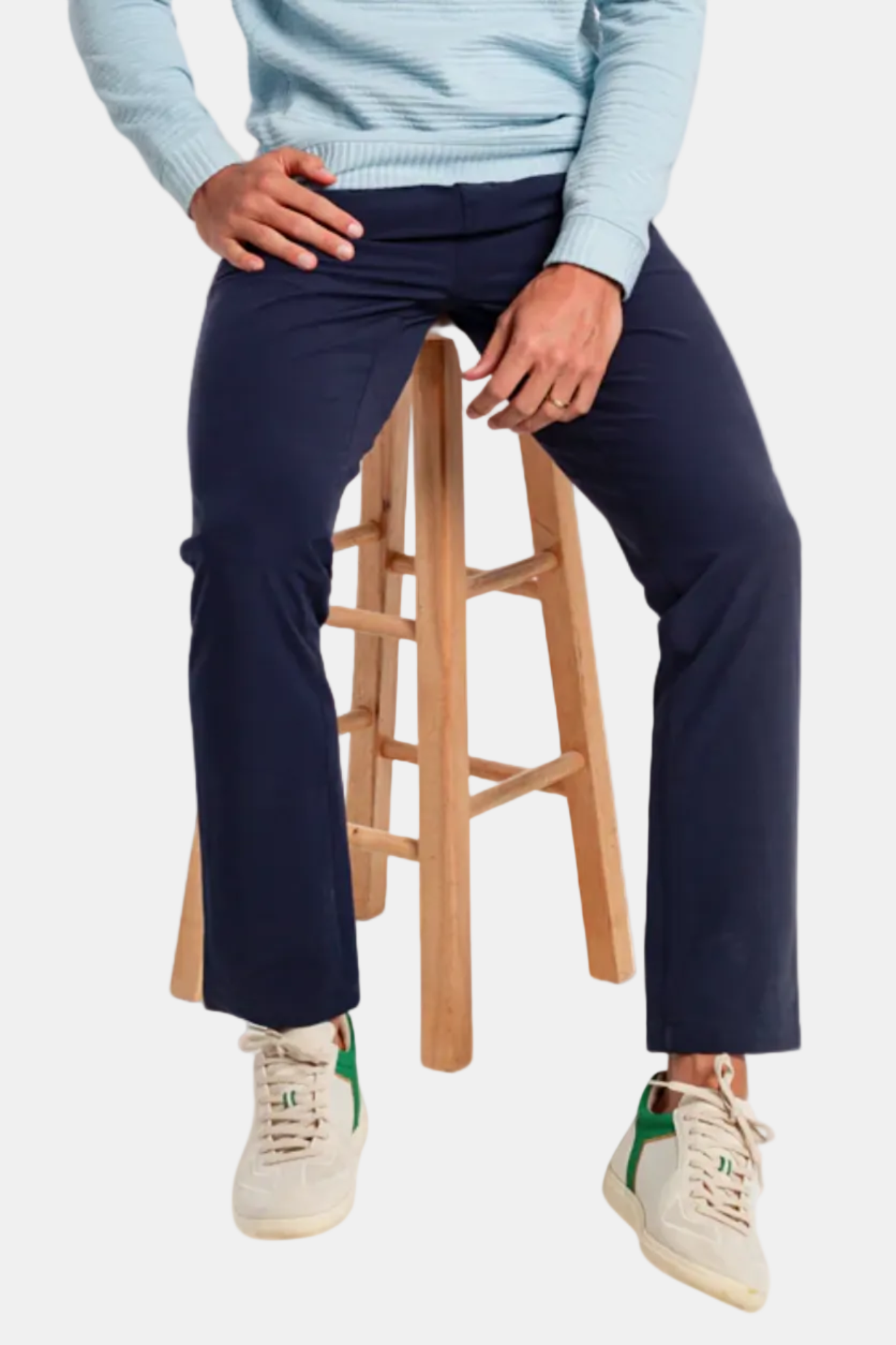 Person wearing navy pants and a light blue sweater sitting on a wooden stool.