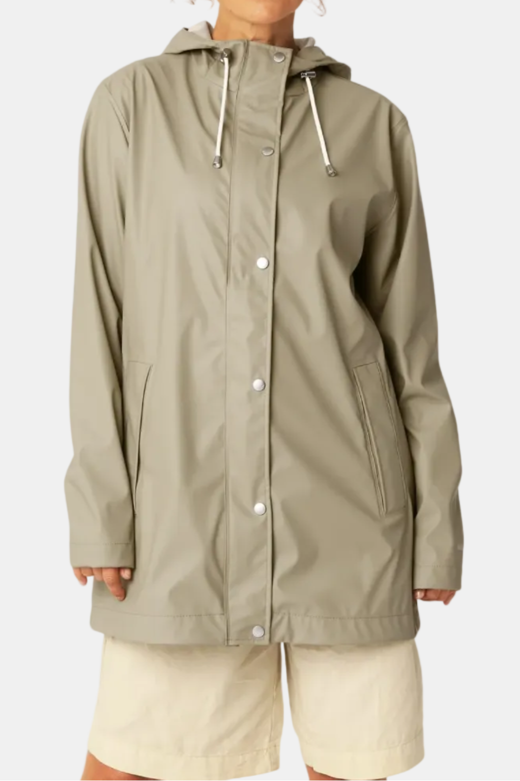 A woman wearing a light olive green hooded raincoat with white drawstrings and beige shorts, standing against a plain light gray studio background.