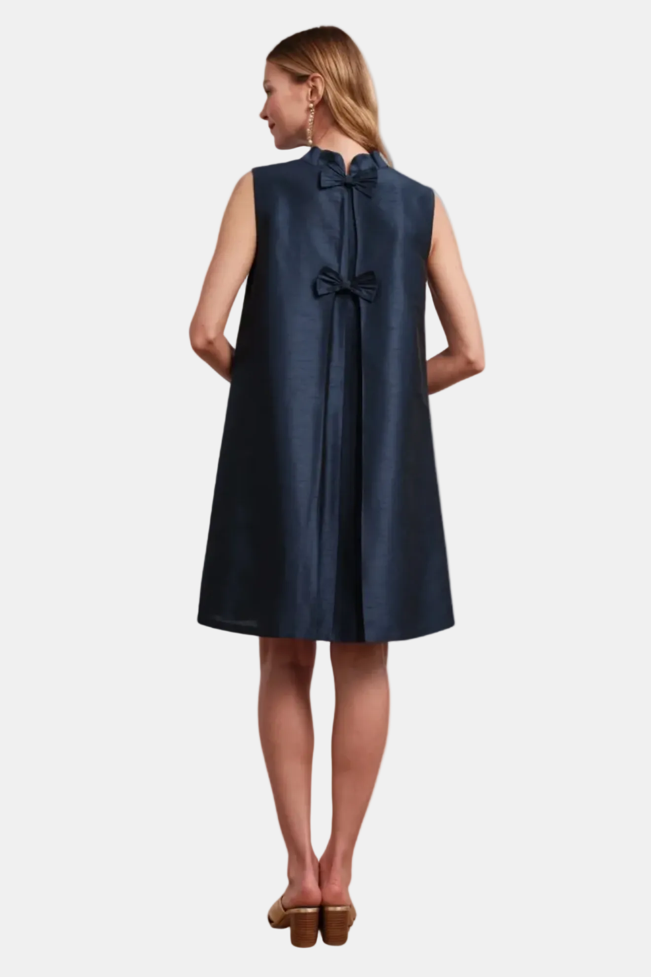 Woman wearing a navy sleeveless dress with a bow detail on a white background