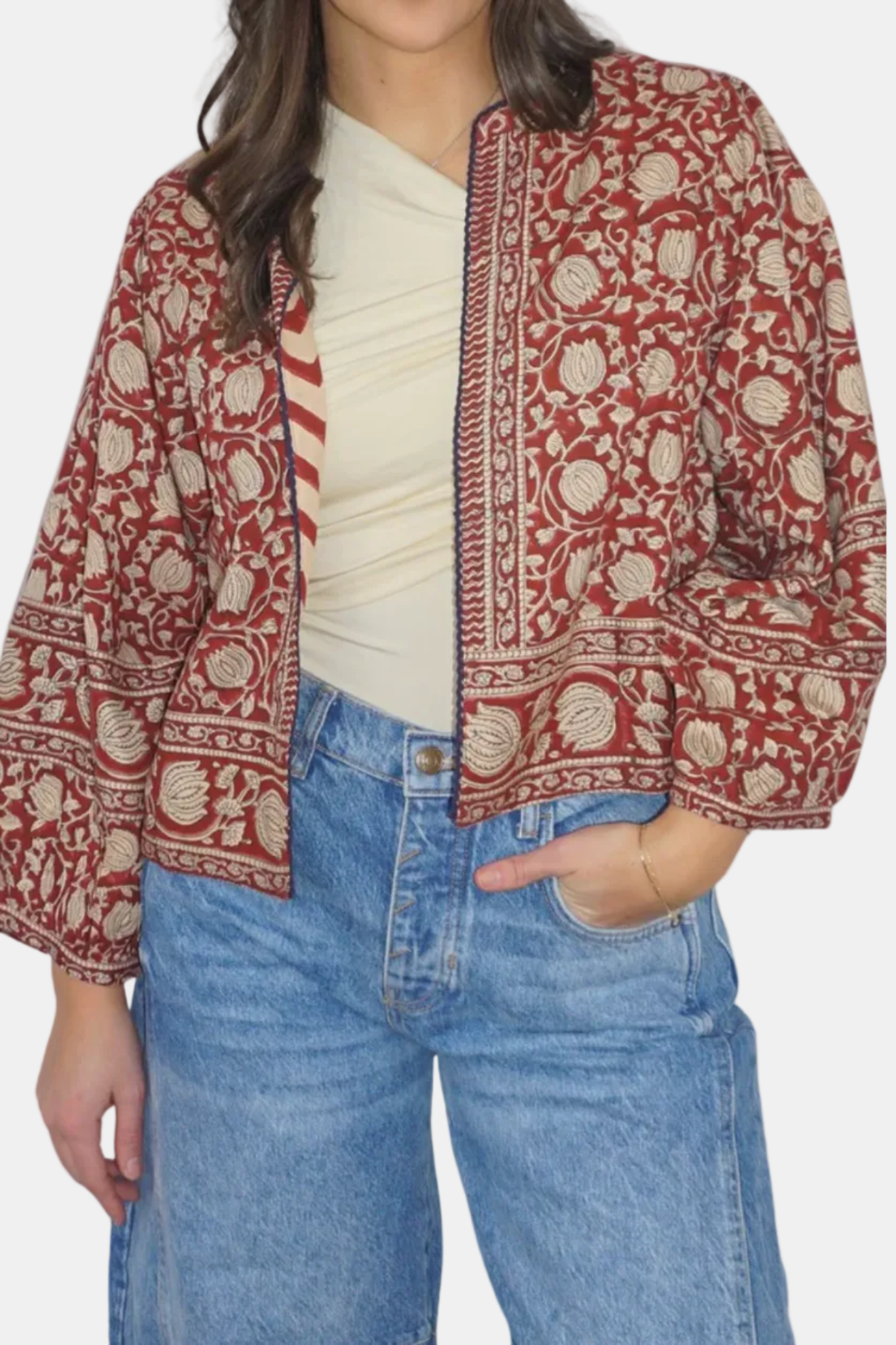 Person wearing a red and beige patterned jacket with blue jeans on a white background
