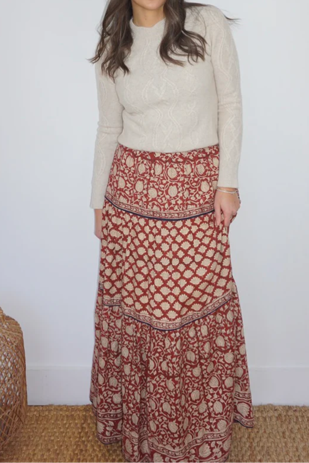 Woman wearing a white sweater and red patterned skirt standing against a plain background