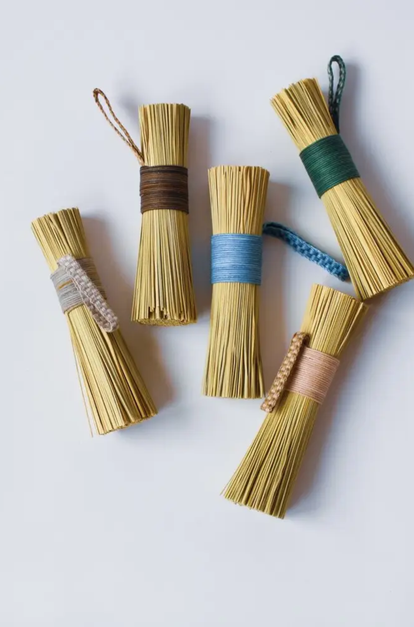 Set of six bundles of dried grass or straw tied with colorful ribbons on a light background