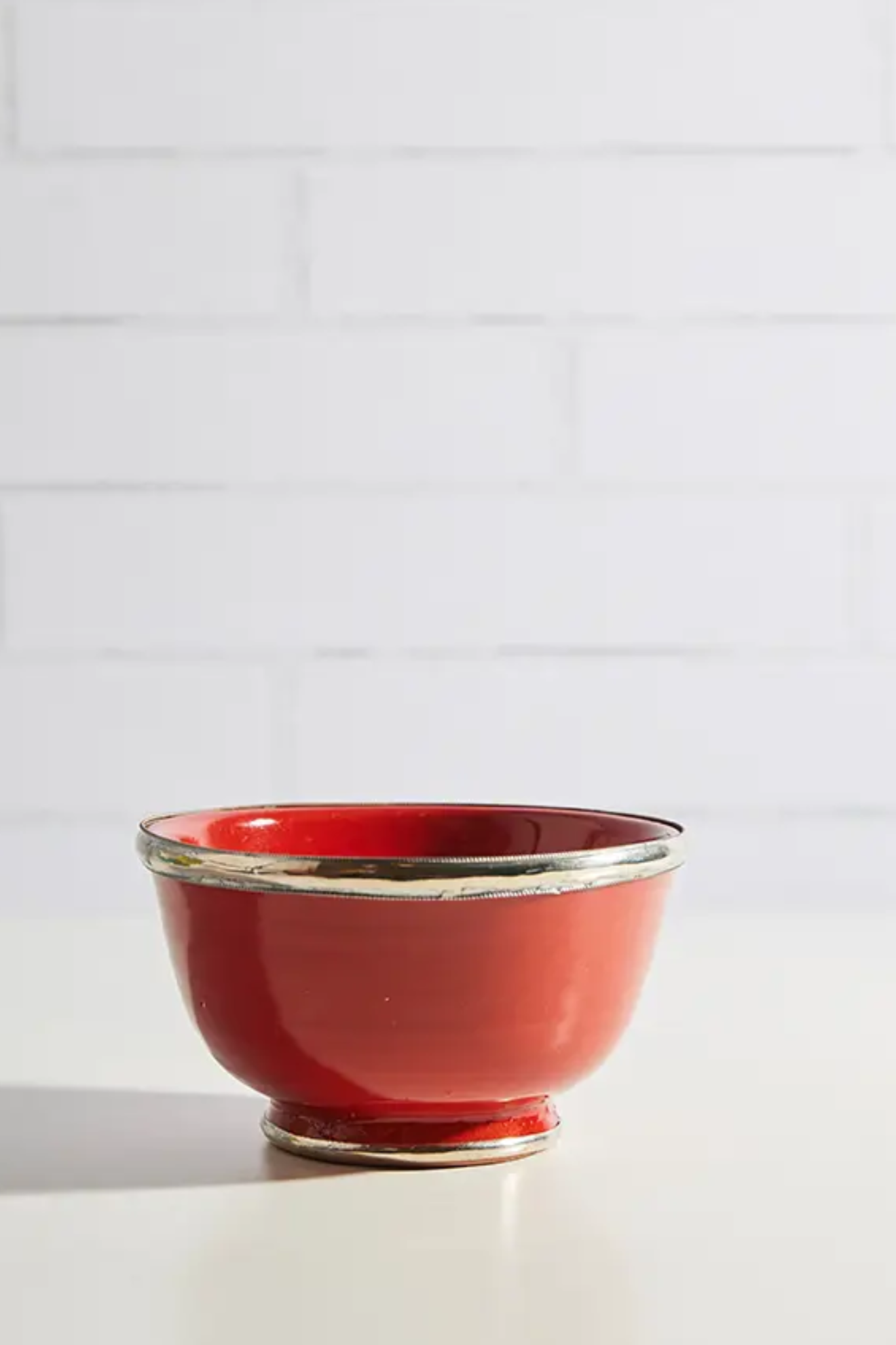 Red ceramic bowl on a white surface with a white tiled wall background