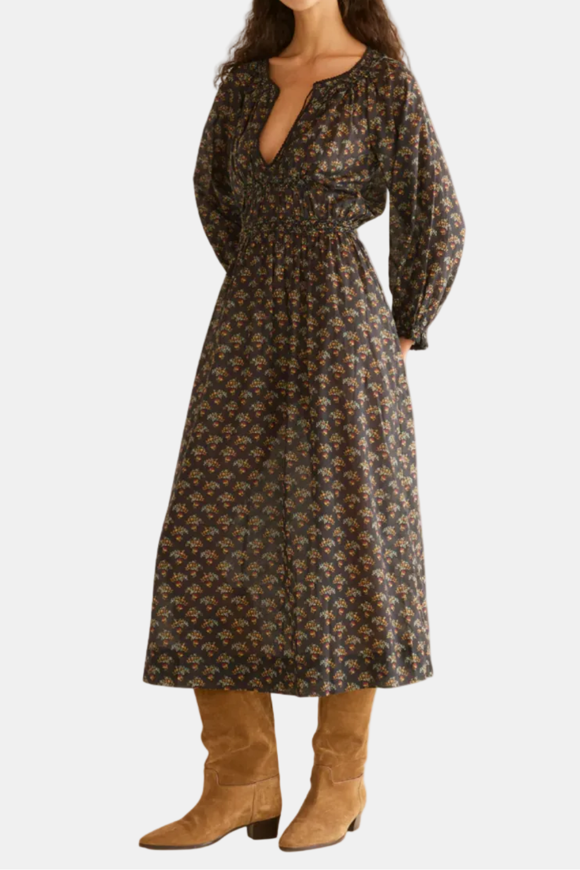 Woman wearing a floral dress with long sleeves and a belt, standing against a white background.