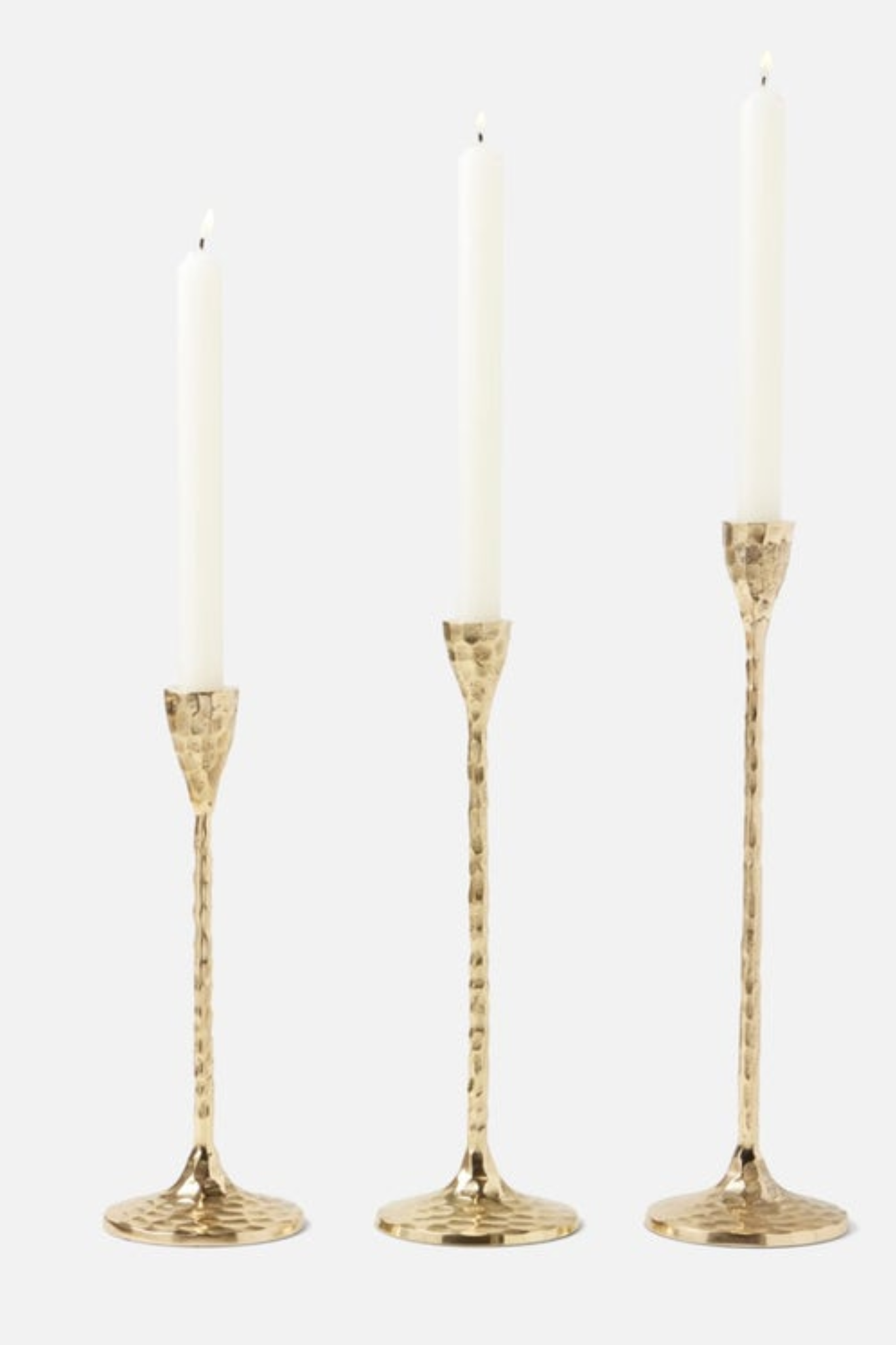 Three gold hammered candle holders with candles on a white background