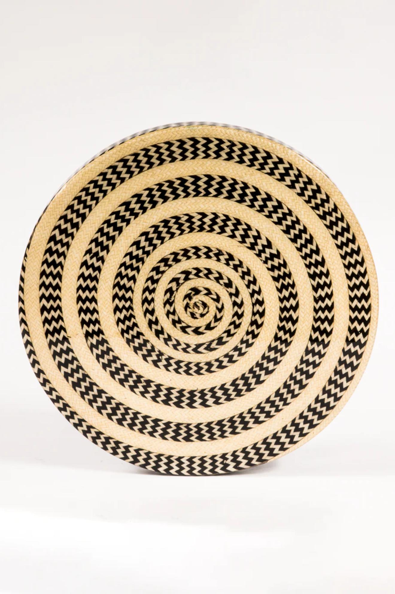 Round woven mat with black and beige spiral pattern on a white background