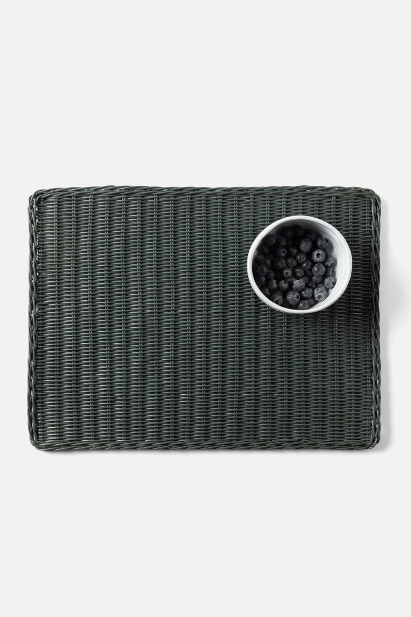 Dark woven placemat with a white bowl of berries on a light gray background