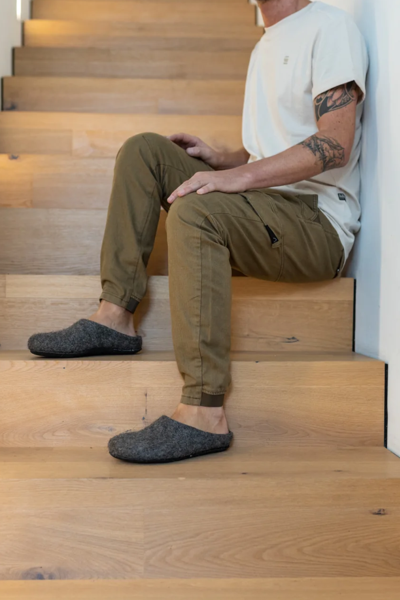Person sitting on wooden stairs wearing brown pants and gray slippers.