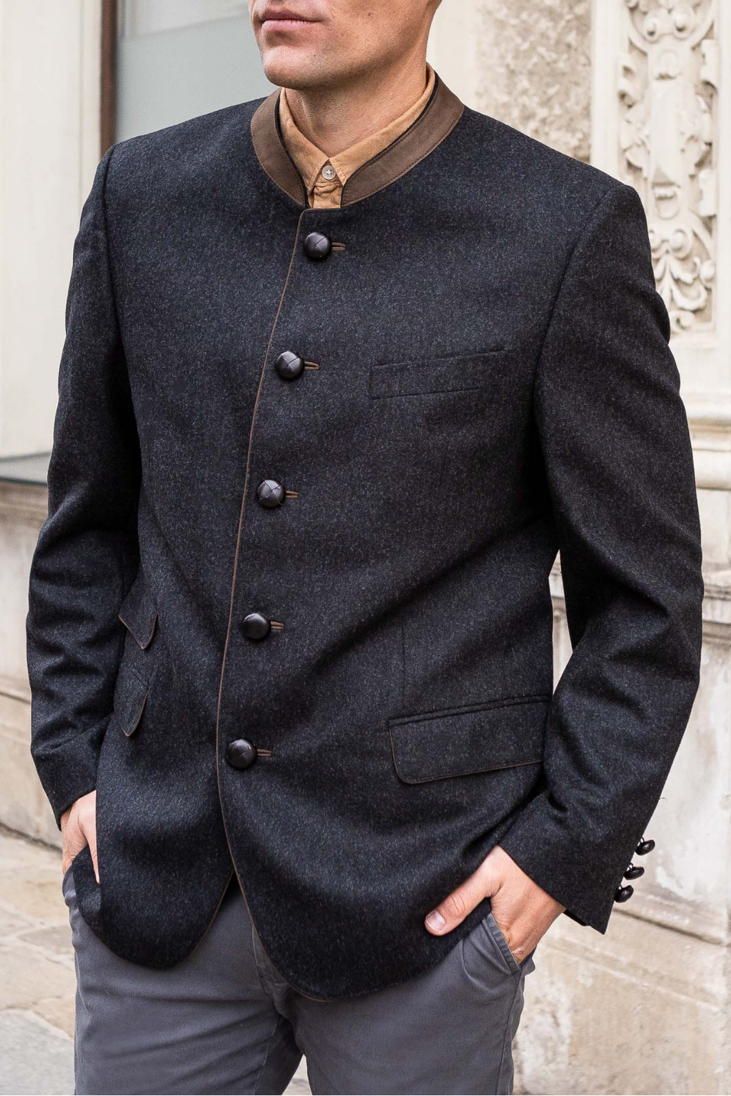 Man wearing a dark blazer with buttons standing against an architectural background