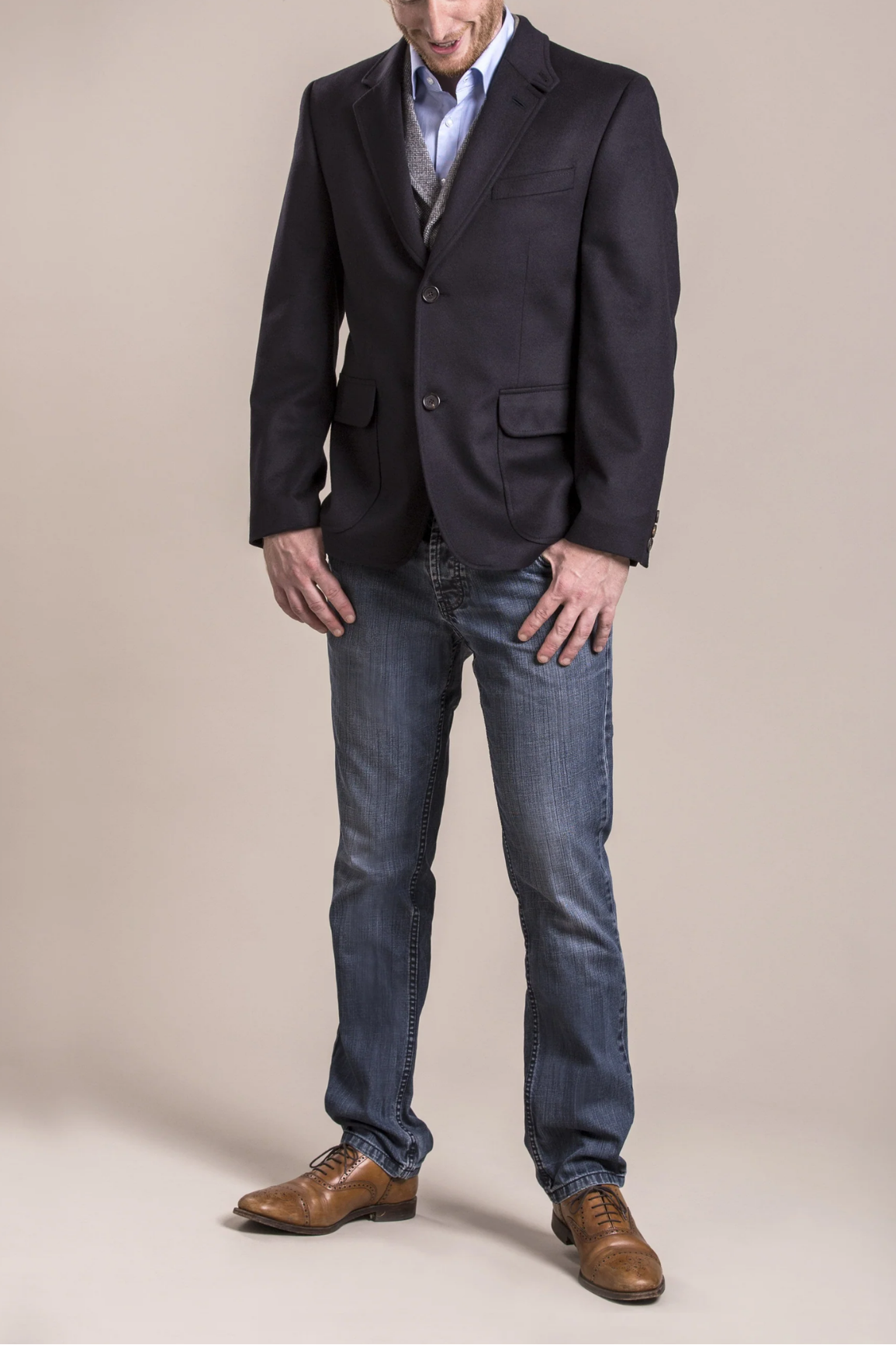 Man wearing a dark blazer, light shirt, and jeans on a beige background
