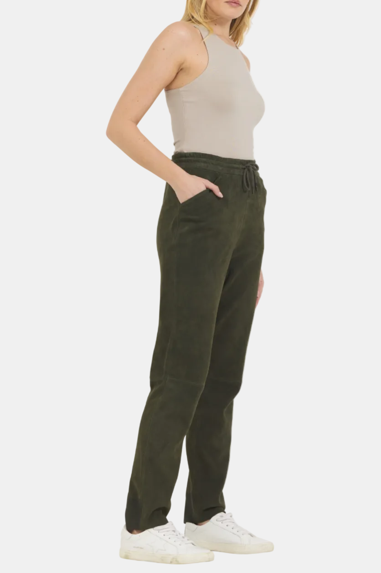 Woman wearing olive green pants and a beige top on a white background