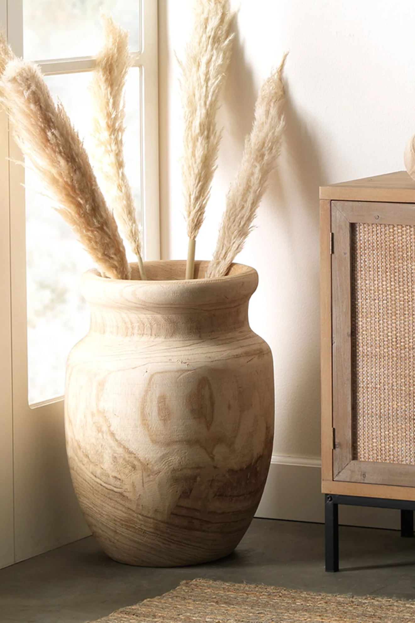 Decorative vase with pampas grass in a room with a window and wooden cabinet.