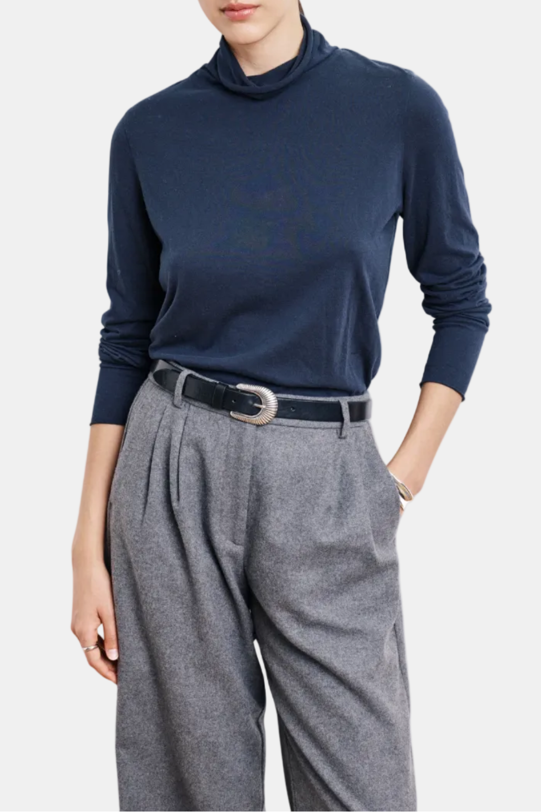 Person wearing a navy turtleneck and gray pleated pants on a white background