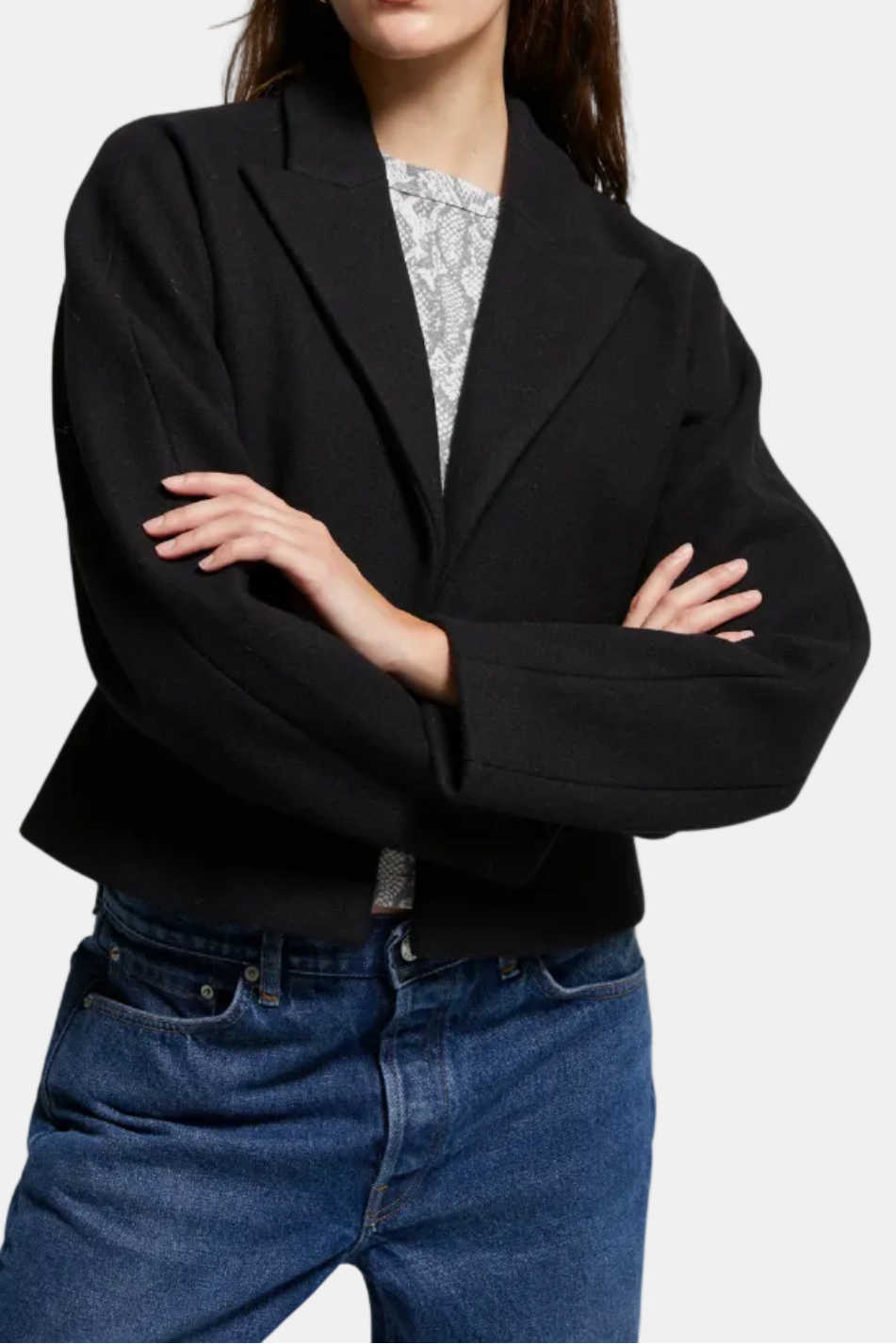 Woman wearing a black blazer, patterned shirt, and blue jeans on a white background