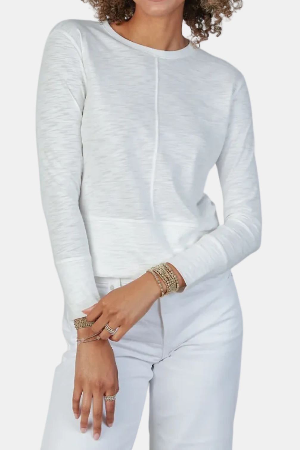 Woman wearing a light gray long-sleeve top and white pants on a white background