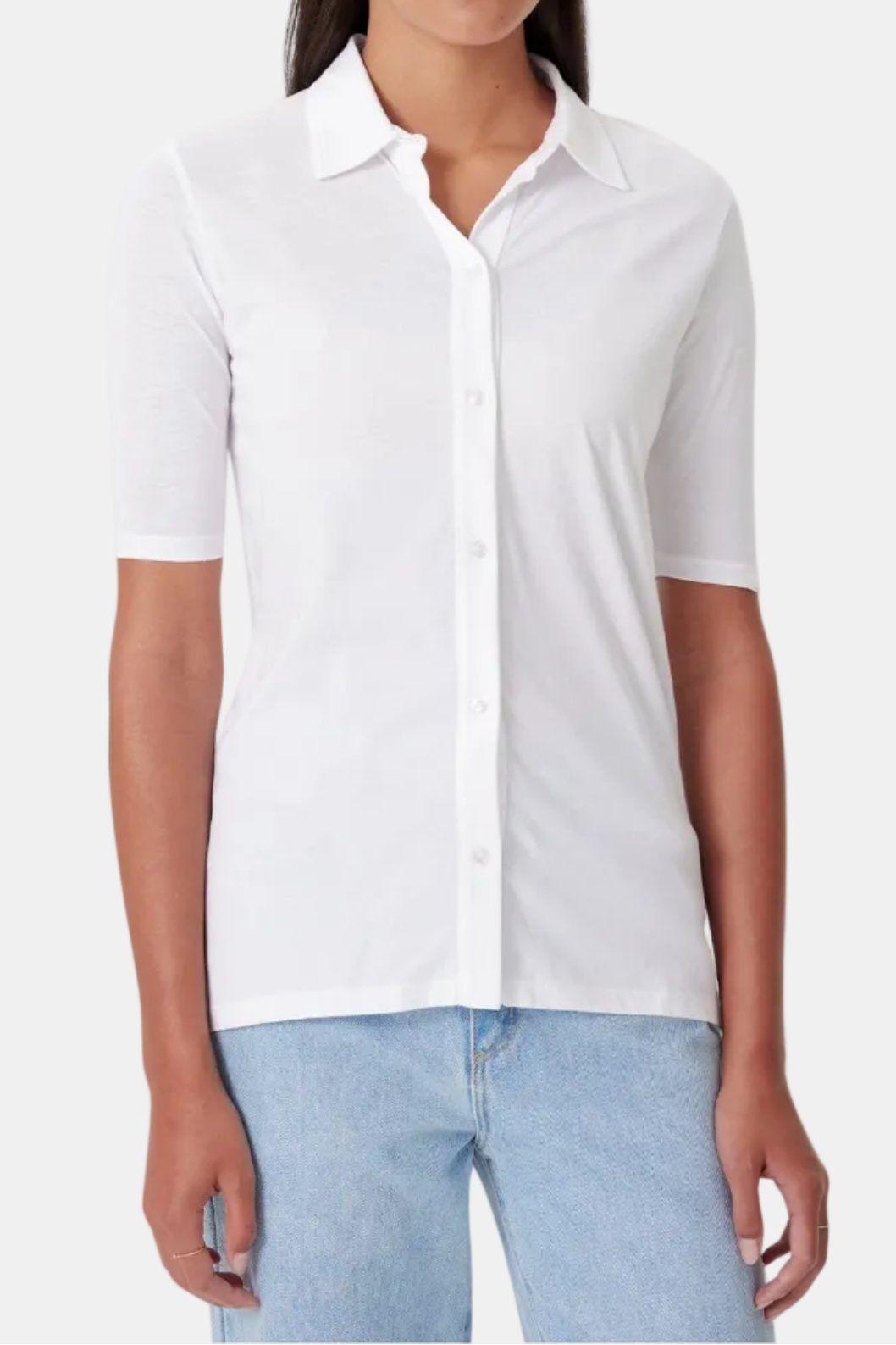 A woman wearing a white, short-sleeved, button-up shirt with a collar, paired with blue jeans.