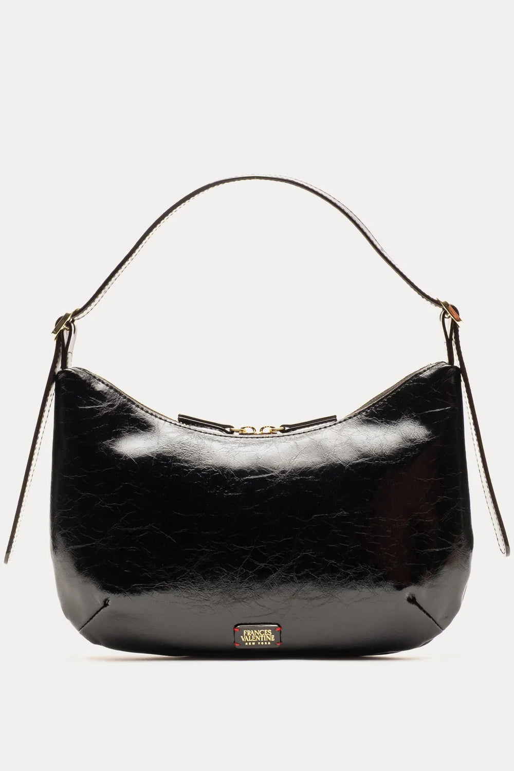 A black patent leather shoulder bag with a curved top, a single leather shoulder strap, and a small gold-tone brand plaque at the bottom center, shown against a light gray background.
