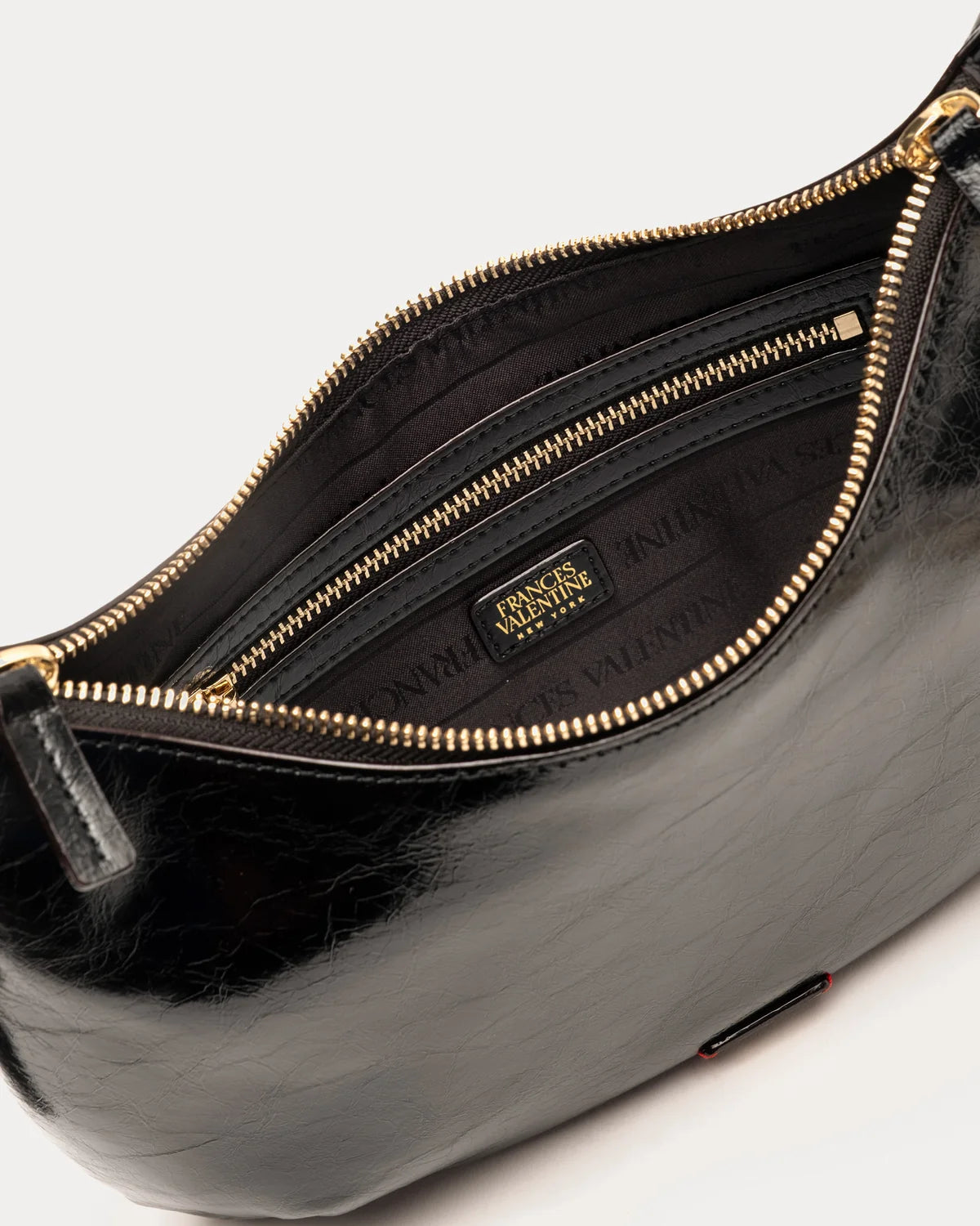 Close-up of a black leather shoulder bag with gold-tone zippers, showing the interior lining and a small black brand plaque that reads Gucci.