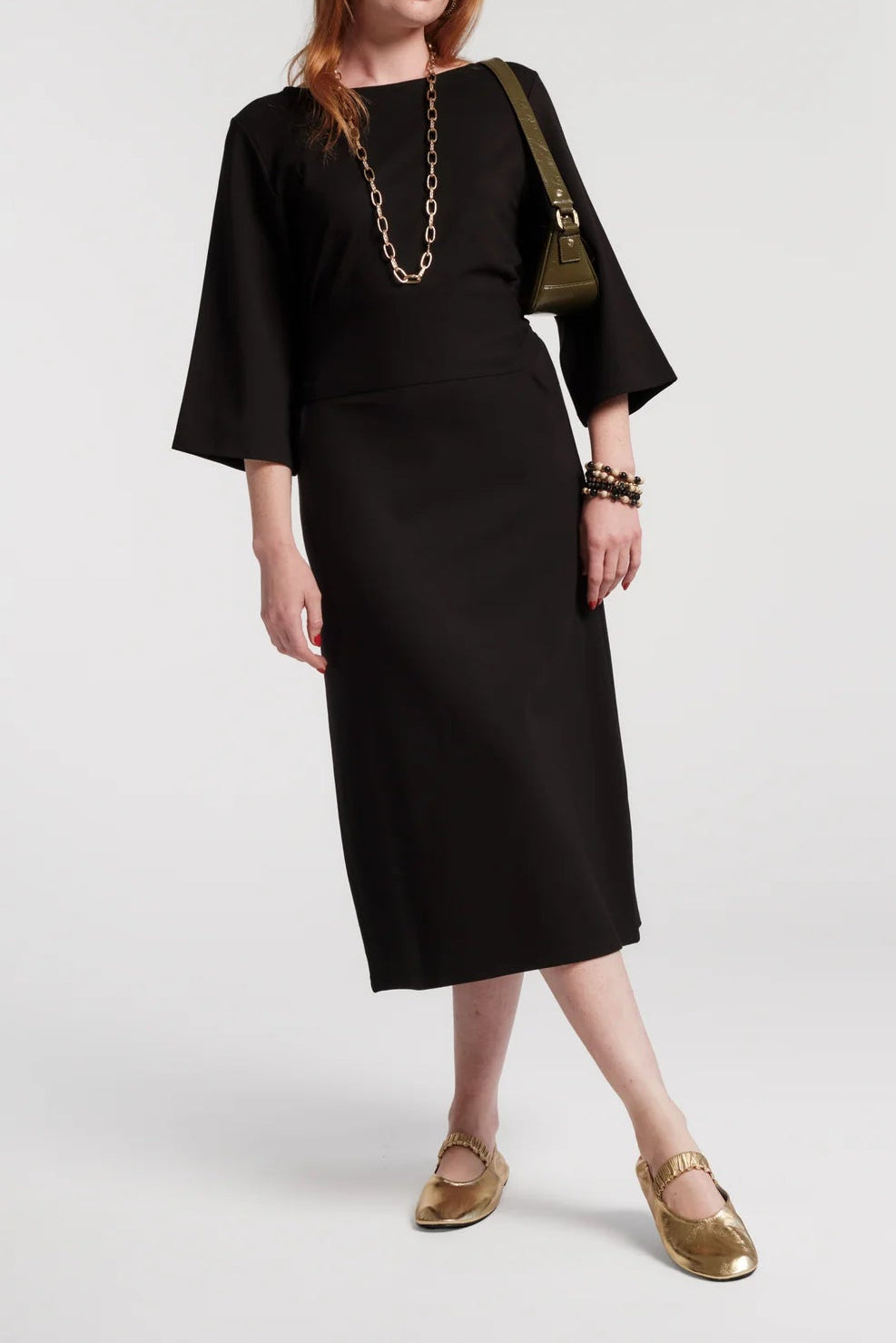 Woman wearing a black dress with gold shoes and bag on a white background