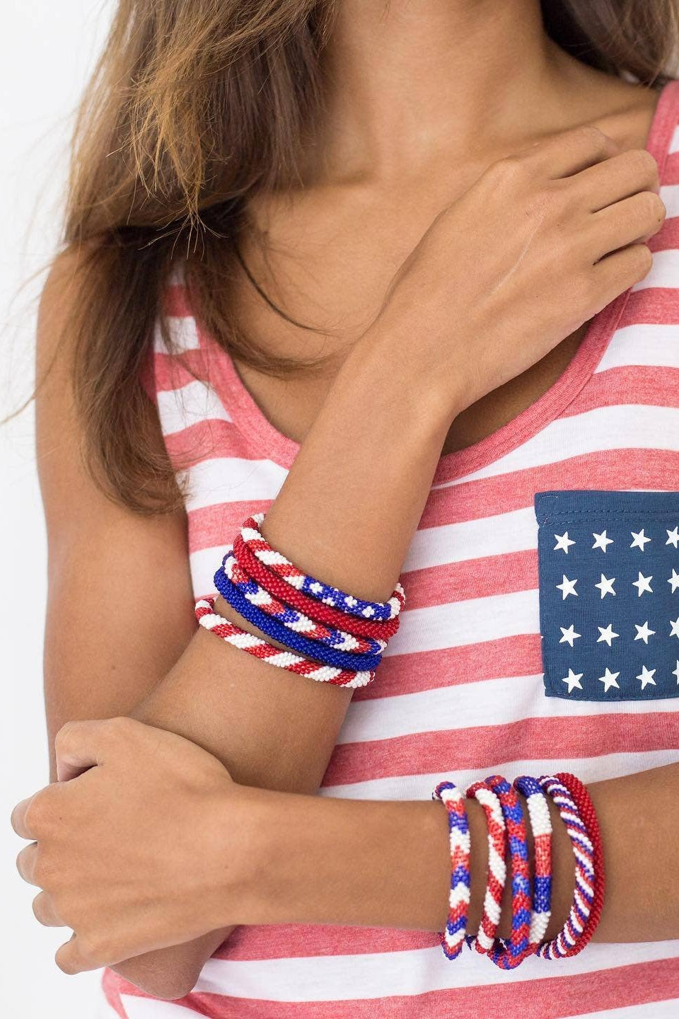 Person wearing a red, white, and blue striped tank top with an American flag design, holding a stack of red, white, and blue bracelets.