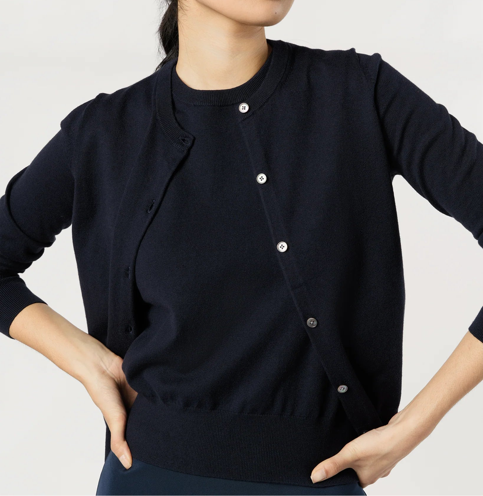 Woman wearing a navy blue cardigan with white buttons on a plain background
