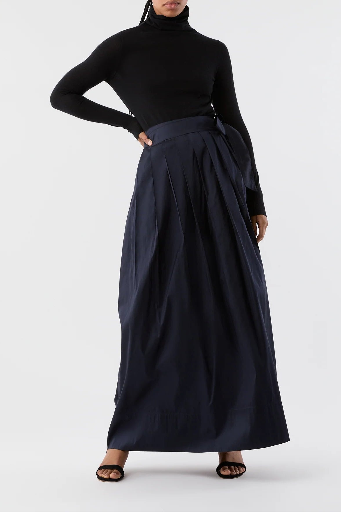 Woman wearing a black turtleneck and long navy skirt on a white background