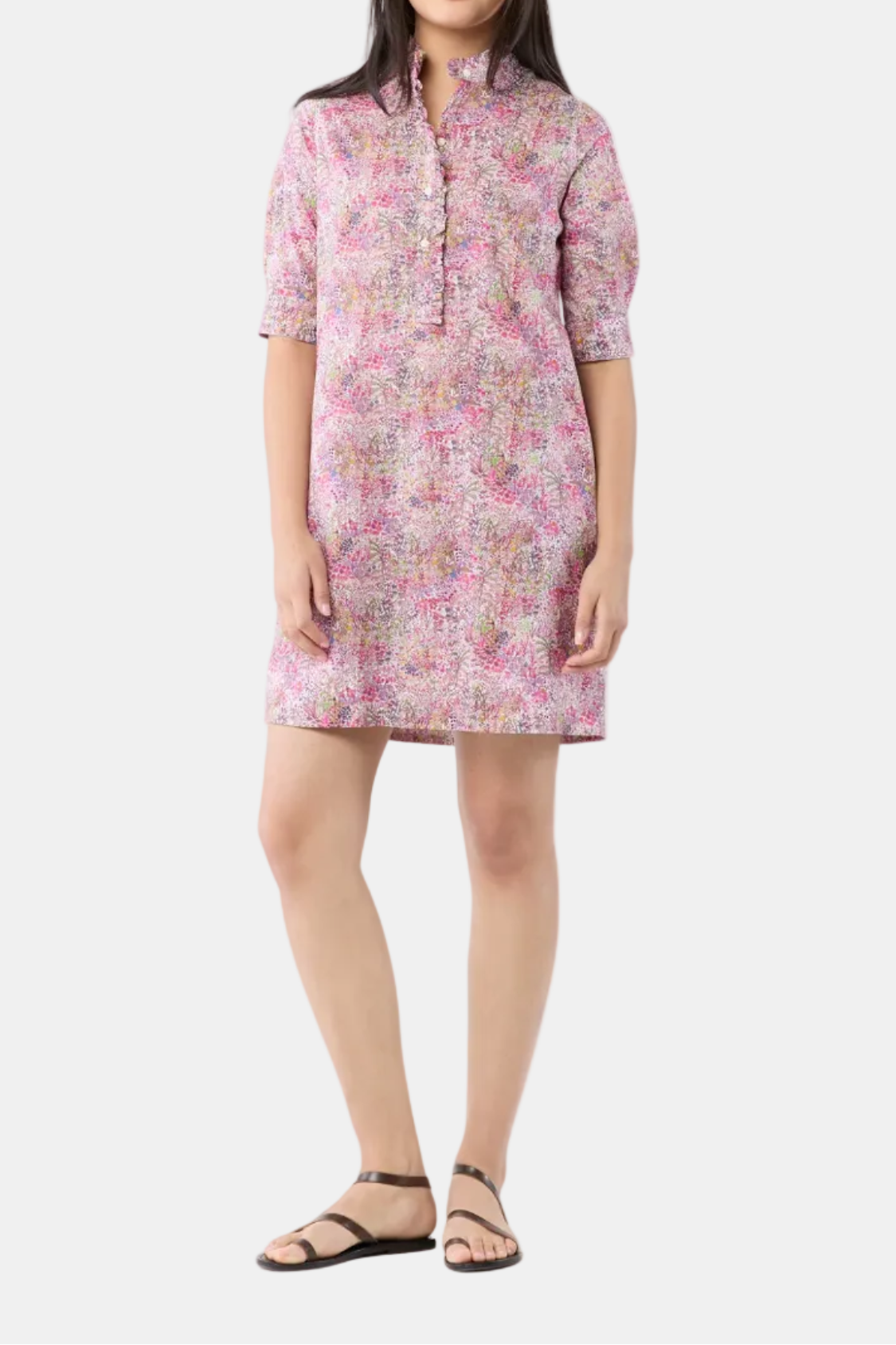 A woman modeling a short-sleeved, high-neck tunic dress with a pink and beige abstract pattern, paired with brown strappy sandals, against a plain white background.