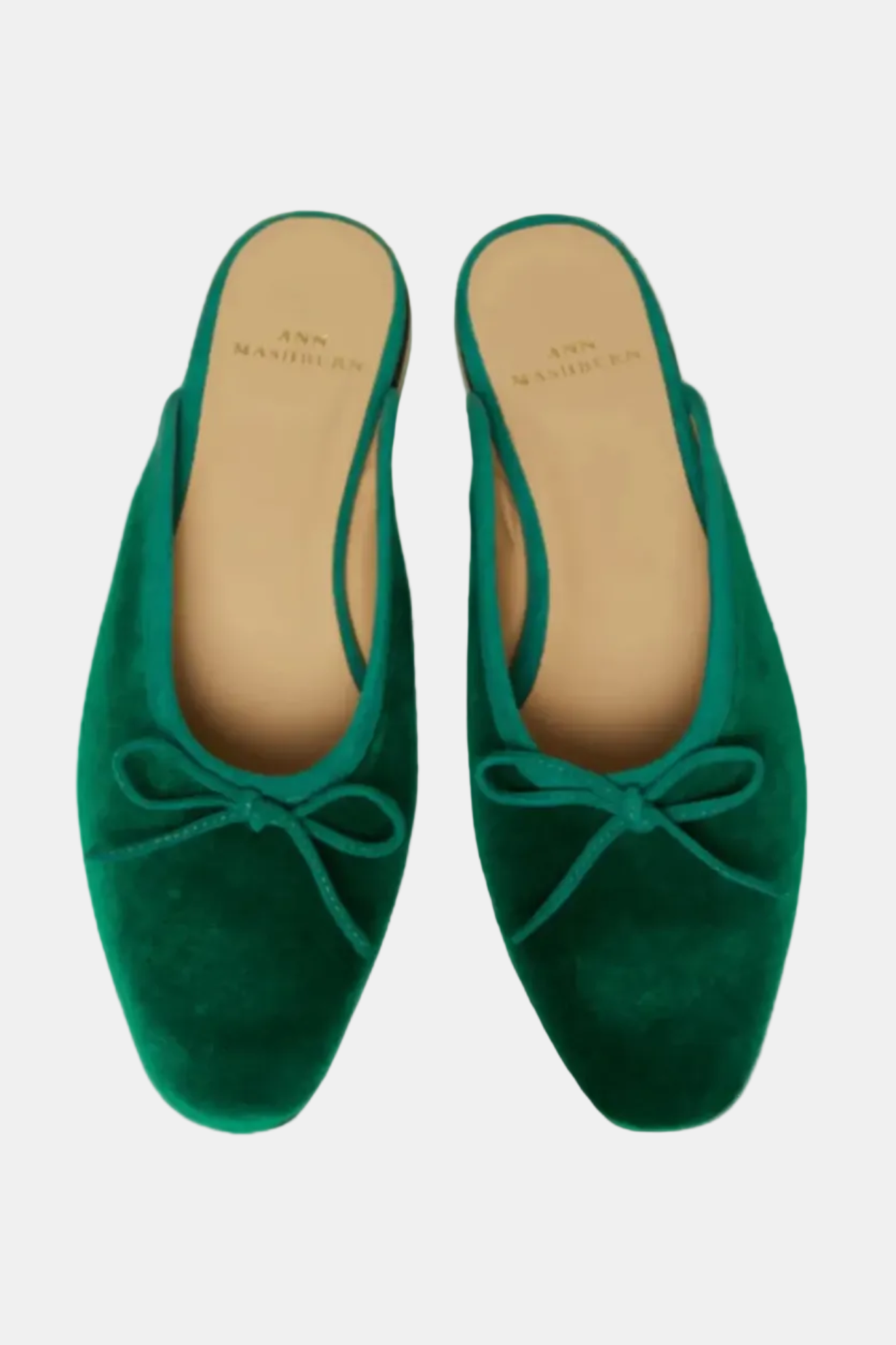 A pair of green velvet mules with a cushioned insole and a bow decoration on the top.