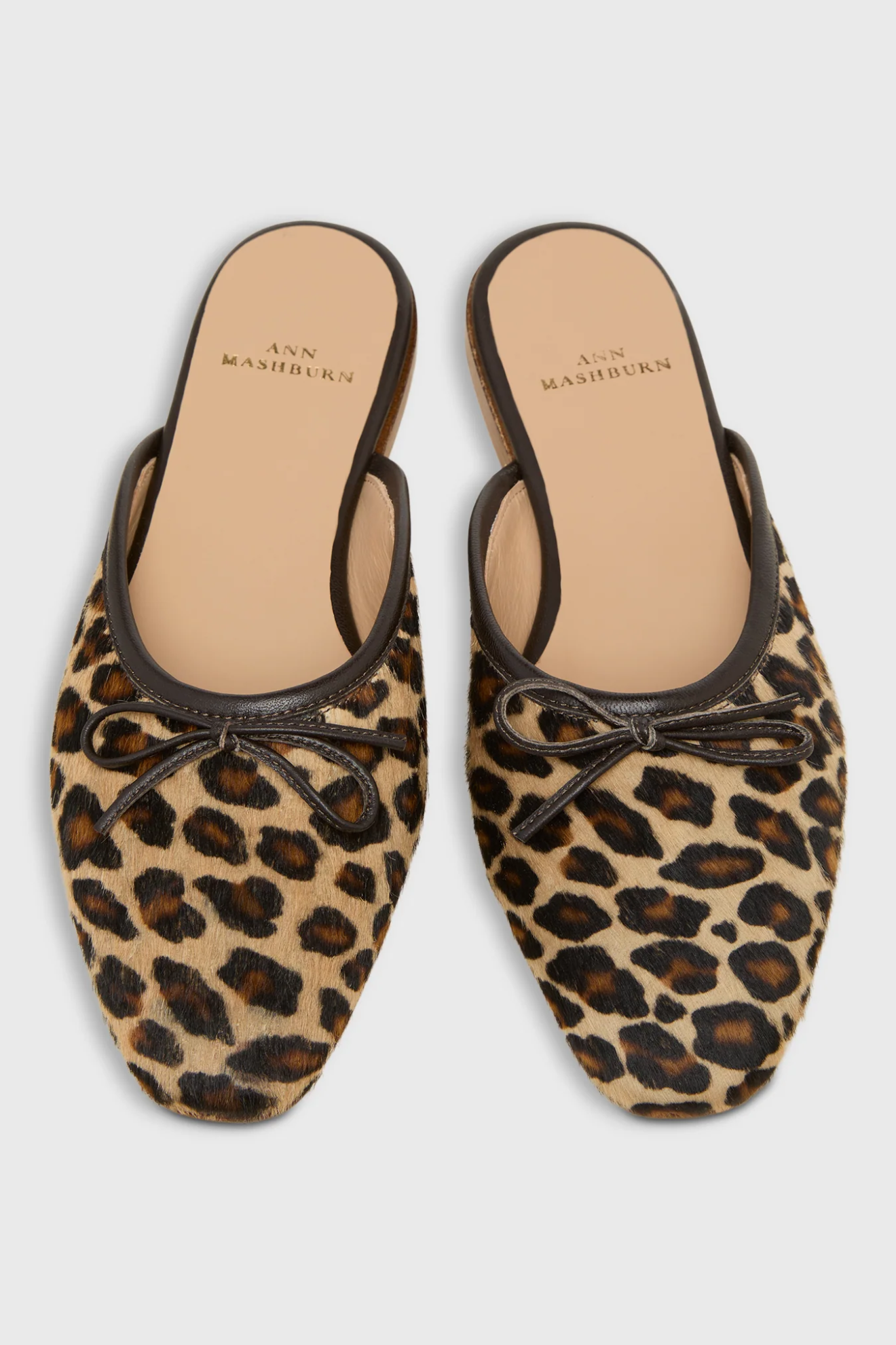 Pair of leopard print shoes with brown leather accents on a light gray background