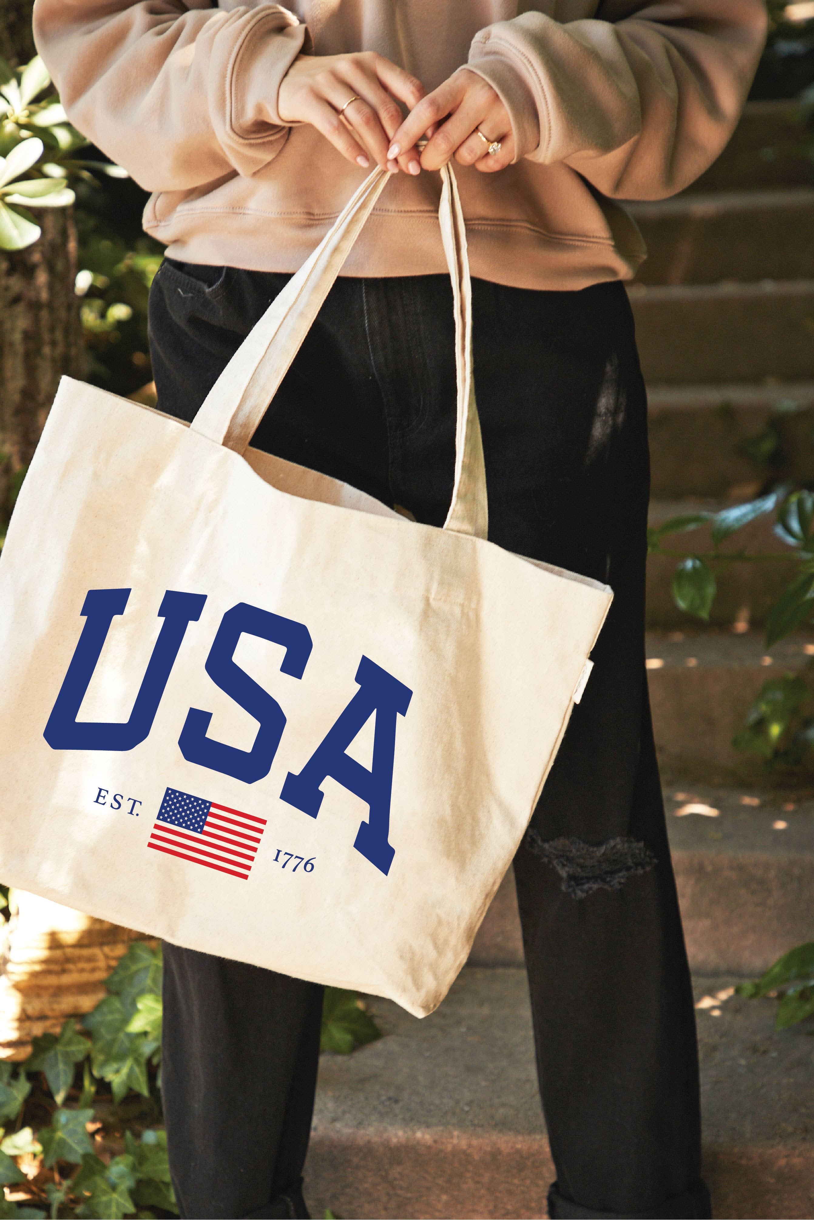 Person holding a tote bag with 'USA' and an American flag design.