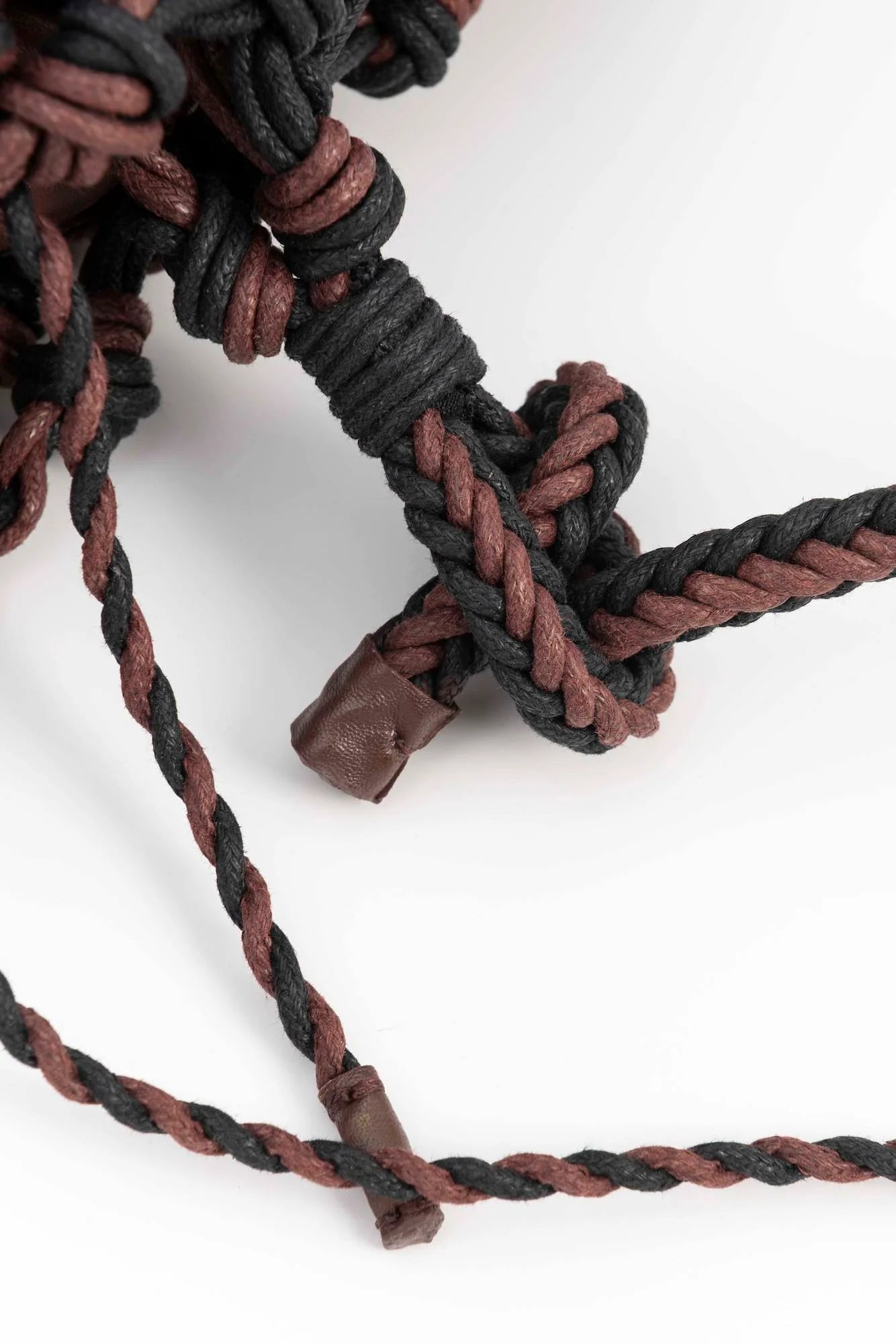 Close-up of a braided rope or cord in dark brown and black, with a knotted section and small brown protective end caps, photographed on a clean white background.