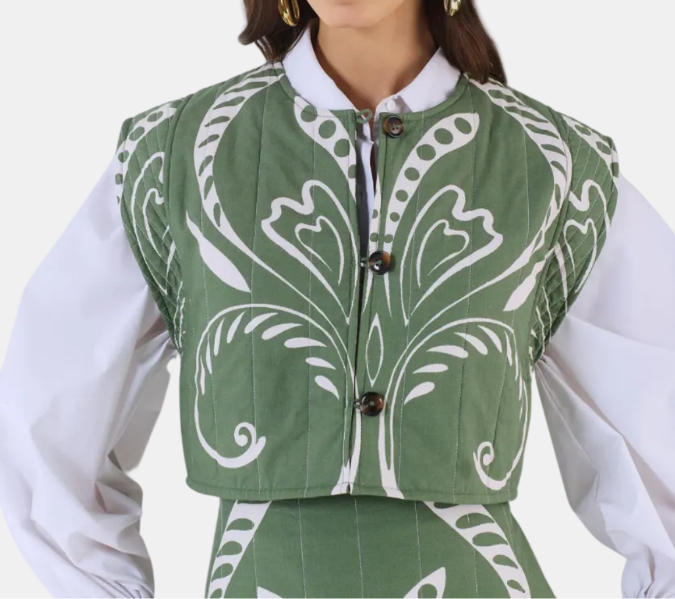 Woman wearing a green patterned vest over a white shirt on a white background