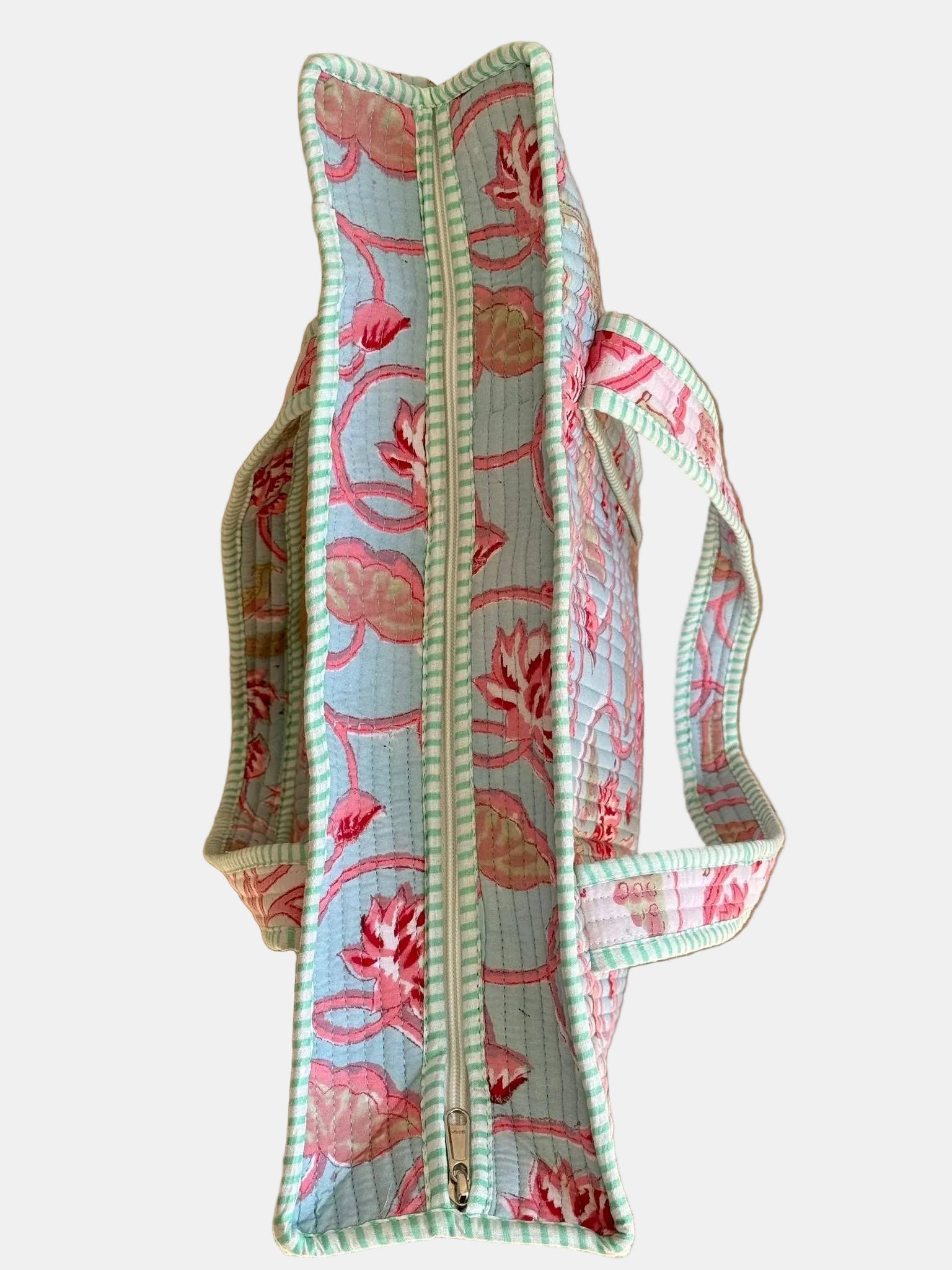 A quilted fabric zippered tote bag with pink floral patterns and a mint green striped border, laid flat on a light wood plank floor.
