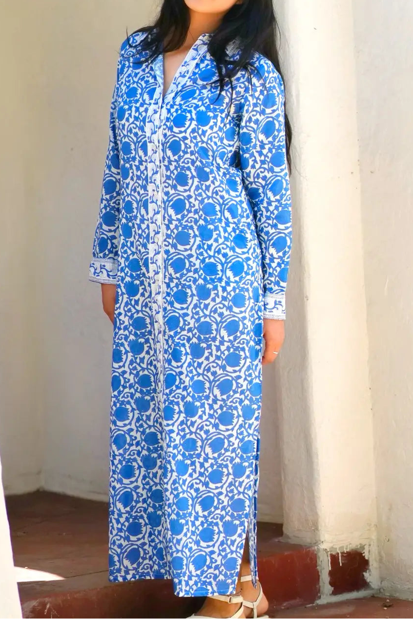 Woman wearing a blue and white patterned dress standing against a white wall.