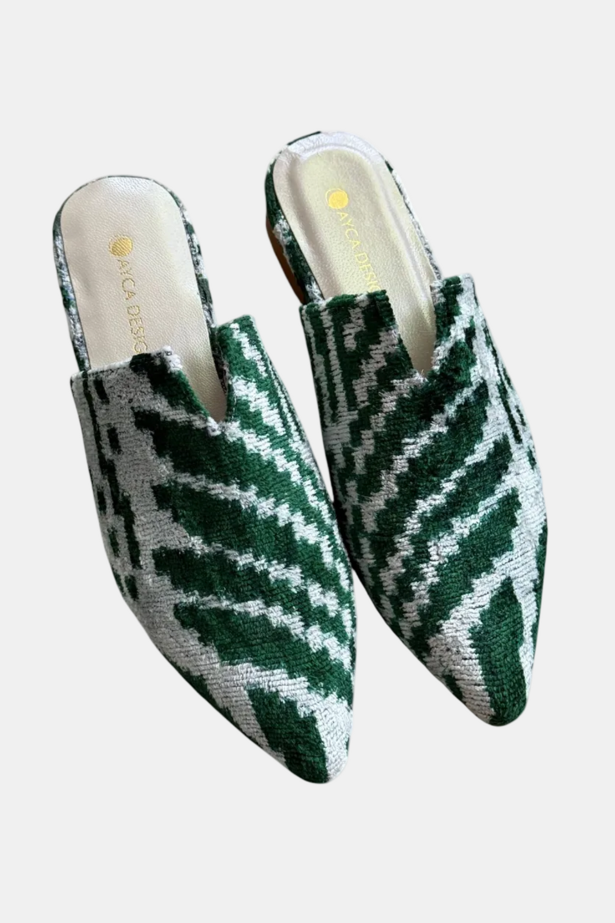 A pair of pointed-toe mule slippers with a green and white geometric ikat pattern, shown against a plain white background. The brand name 'KICA DESIGNS' is visible on the insole.