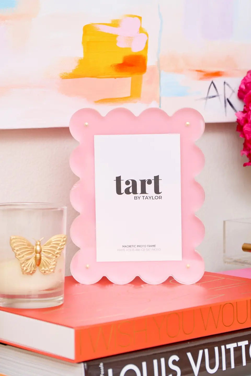 Pink 'tart' by Taylor frame on books with a candle and flowers in the background